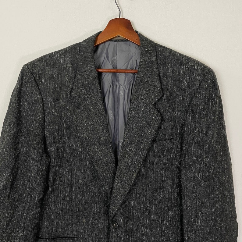 Op de afbeelding: Een donkergrijze blazer met een subtiel textuurpatroon. De blazer heeft een enkele knoopsluiting en een revers.