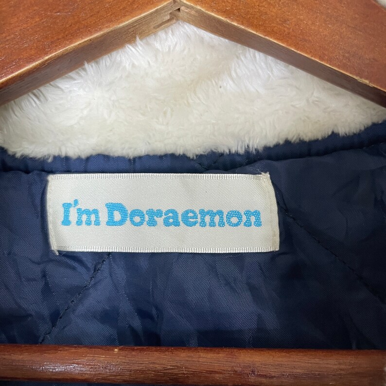 Może przedstawiać: Zbliżenie na niebieską kurtkę z białą metką z napisem "I'm Doraemon".