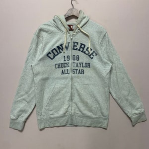 Op de afbeelding: Een lichtgrijze hoodie met rits en een Converse-logo en de tekst "19 08 Chuck Taylor All Star".