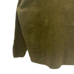May include: Olive green long-sleeve shirt. The fabric appears to be a soft, textured material. The shirt has a simple, classic design, with a crew neck and long sleeves. The overall look is casual and comfortable.