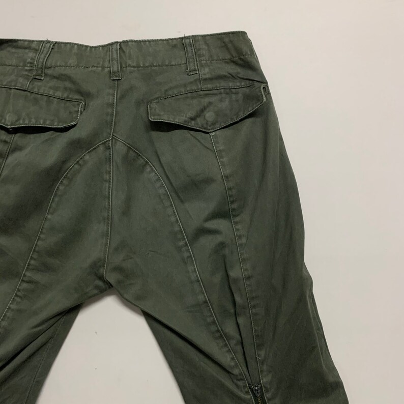 May include: A pair of dark green cargo pants with a zipper at the bottom of the legs. The pants have a back pocket on the right side.