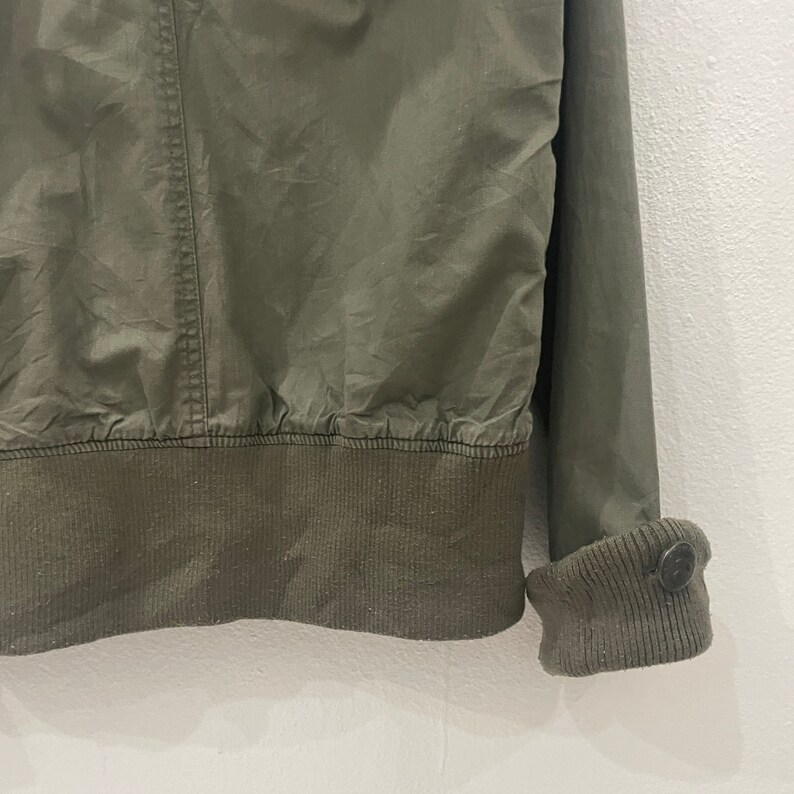 May include: A green cotton jacket with a ribbed knit collar, cuffs, and waistband. The jacket has a zipper closure and two pockets.