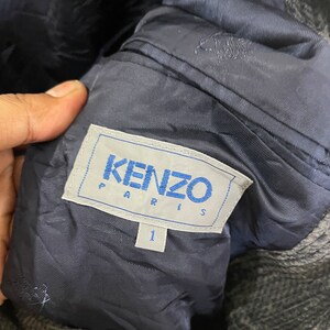 以下が含まれることがあります： 黒とグレーのジャケットに、青いKENZO PARISのラベルとサイズ1のタグが付いている。