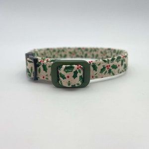 May include: A green and white patterned cat collar with a green buckle. The pattern features holly leaves and red berries.