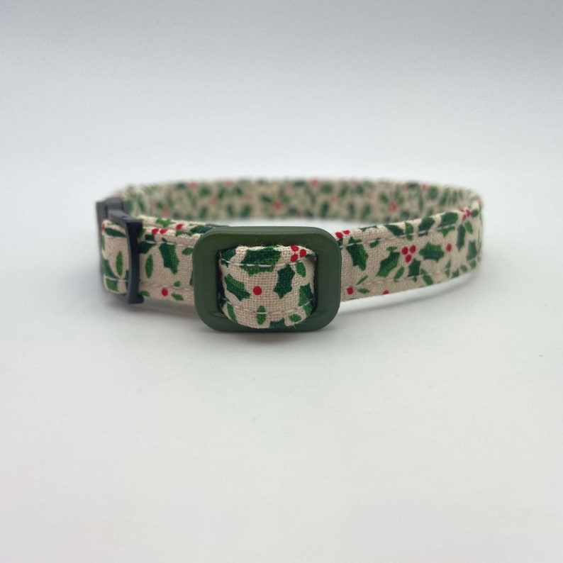May include: A green and white patterned cat collar with a green buckle. The pattern features holly leaves and red berries.