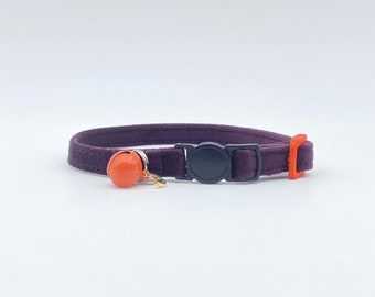 May include: A purple velvet cat collar with a black buckle and an orange bell. The collar is designed for cats and has a breakaway buckle for safety.