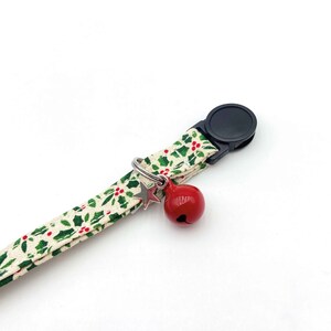 May include: A white and green patterned cat collar with a red bell and a silver star charm. The collar has a black plastic buckle.