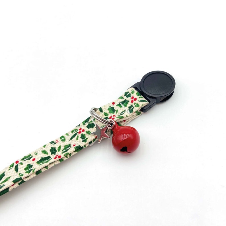 May include: A white and green patterned cat collar with a red bell and a silver star charm. The collar has a black plastic buckle.