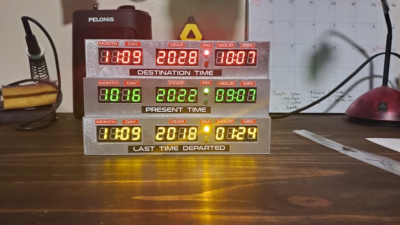 May include: A silver-colored time machine prop with three stacked displays. Each display has a digital readout for month, day, year, AM/PM, hour, and minute. The top display reads "88:09 2028 10:08" and is labeled "Destination Time". The middle display reads "88:88 2028 08:08" and is labeled "Present Time". The bottom display reads "88:09 2088 08:29" and is labeled "Last Time Departed".