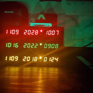 May include: A black digital clock with a red, green, and yellow display. The clock shows the date and time. The date is 10-16-2022 and the time is 09:08. The clock also shows the date 11-09-2018 and the time 01:24.