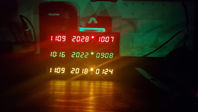 May include: A black digital clock with a red, green, and yellow display. The clock shows the date and time. The date is 10-16-2022 and the time is 09:08. The clock also shows the date 11-09-2018 and the time 01:24.