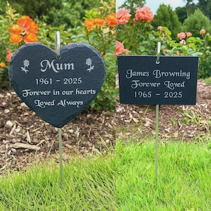 May include: Two dark grey slate memorial markers on metal stakes. The heart-shaped marker reads Mum, 1961-2025, Forever in our hearts, Loved Always with rose icons. The rectangular marker reads James Browning, Forever Loved, 1965-2025.