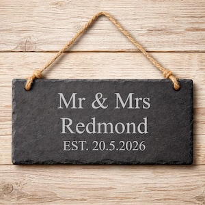 A rectangular dark grey slate plaque hangs by a twine rope against a wooden background, engraved with Mr & Mrs Redmond and EST. 20.5.2026.