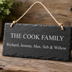 A rectangular grey slate sign hangs by a rope against a wooden surface, engraved with the text THE COOK FAMILY above Richard, Jemma, Max, Seb & Willow.