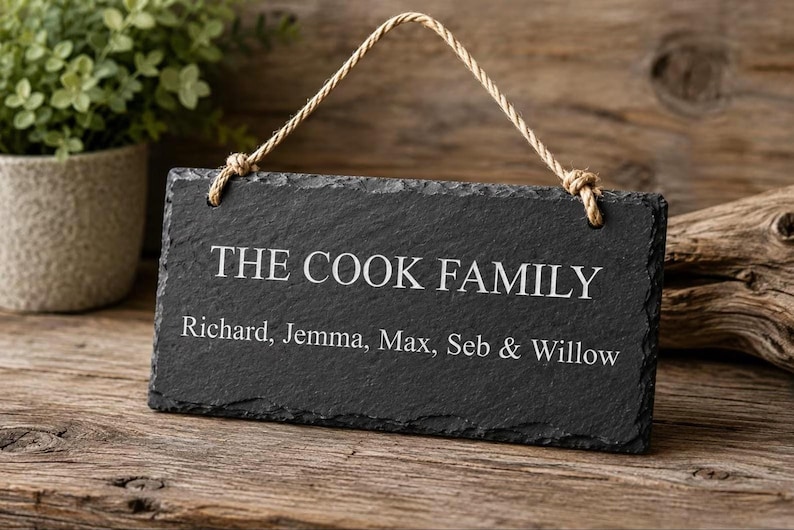 A rectangular grey slate sign hangs by a rope against a wooden surface, engraved with the text THE COOK FAMILY above Richard, Jemma, Max, Seb & Willow.
