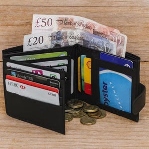An open black leather wallet on a wooden surface holding British banknotes, various cards, and coins.
