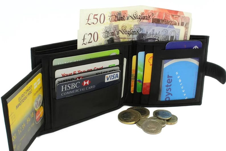 An open black leather wallet filled with credit cards, British pound banknotes, and coins scattered in front.