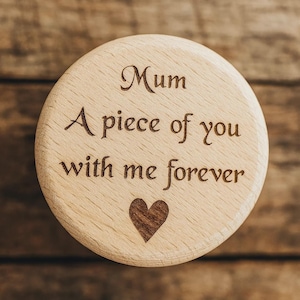 May include: A circular wooden keepsake engraved with the words "Mum, A piece of you with me forever". A heart is carved below the text. The keepsake is light brown and rests on a wooden surface.