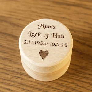 Könnte beinhalten: Kleine, runde Holzkiste mit Deckel. Der Deckel ist mit den Worten „Mum's Lock of Hair“, Daten und einem Herzsymbol graviert. Die Kiste ist aus hellem Holz gefertigt.