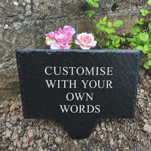 Könnte beinhalten: Ein rechteckiges Gartenschild aus schwarzem Schiefer mit einem spitz zulaufenden Erdspieß. Die Oberfläche zeigt den eingravierten weißen Text CUSTOMISE WITH YOUR OWN WORDS in einer klaren Schriftart. Das Schild hat eine raue Natursteintextur.