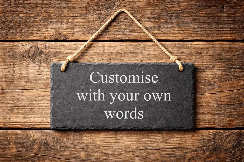 A rectangular dark grey slate plaque hanging by a rustic twine rope against a horizontal wood plank background, featuring the laser-engraved text Customise with your own words.