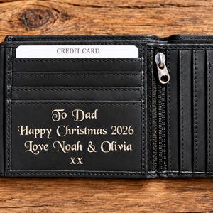 May include: A black leather bifold wallet with multiple card slots and a zippered compartment. The interior features an engraving that reads: To Dad, Happy Christmas 2026, Love Noah & Olivia, XX. A white credit card is inserted into the top slot.