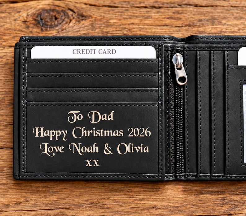 May include: A black leather bifold wallet with multiple card slots and a zippered compartment. The interior features an engraving that reads: To Dad, Happy Christmas 2026, Love Noah & Olivia, XX. A white credit card is inserted into the top slot.