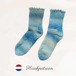Op de afbeelding: Een paar handgemaakte sokken met een blauw-groen verloop. De sokken hebben een geschulpte rand aan de bovenkant en zijn gemaakt van getextureerd garen. De tekst "Haakpatroon" is zichtbaar.