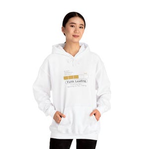 Puede incluir: Sudadera con capucha blanca con bolsillo delantero y cordón. La sudadera presenta el texto "Faith Loading" en color dorado, junto con las palabras "prayer... obedience... patience..." y "Trusting God... waiting on His Timing."