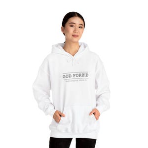 May include: White hooded sweatshirt with the text "GOD FORBID" above "Still praying about it." in black. The sweatshirt has a front pocket and a drawstring hood. The model is wearing black pants.