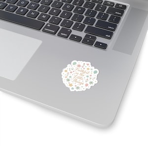 May include: A white sticker with the text "Faithful in the Little Things" in a whimsical font. The sticker is decorated with pastel-colored floral and star designs, and is placed on a laptop.