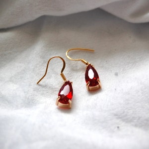 May include: A pair of gold earrings with teardrop-shaped red gemstones.