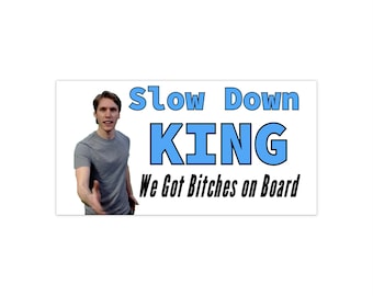 May include: A white sign with blue text that reads "Slow Down King We Got Bitches on Board". A man in a grey shirt is pictured on the left side of the sign.