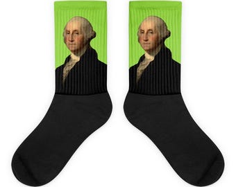 May include: A pair of black socks with a green background featuring a portrait of George Washington.