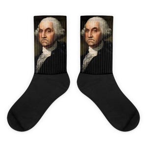 May include: A pair of black socks with a portrait of George Washington on the front. The portrait is in color and shows Washington with a serious expression.