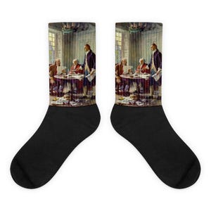 May include: Pair of black socks featuring a historical painting of men in colonial attire gathered around a table. The artwork depicts a meeting in a room with windows and a chandelier. The socks are a unique accessory.
