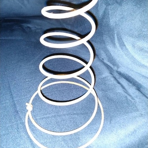 May include: A white metal spring coil, commonly used in furniture, is shown against a blue background.