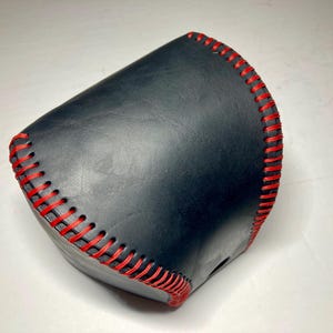 May include: A black leather item with red stitching. The item has a curved shape and appears to be handmade. The red stitching provides a striking contrast against the black leather.
