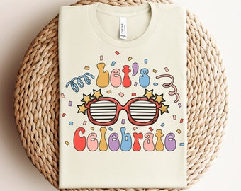 May include: A light beige t-shirt featuring the text "Let's Celebrate" in colourful letters and a pair of red sunglasses with gold stars on the side. The text is surrounded by confetti.