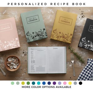 Può includere: Una collezione di libri di ricette personalizzati in vari colori, tra cui rosa, verde, giallo e nero. Ogni libro presenta un design unico con illustrazioni botaniche e la scritta "COOKBOOK". È visibile anche un libro di ricette aperto, insieme a una ciotola di conchiglie e una forchetta.