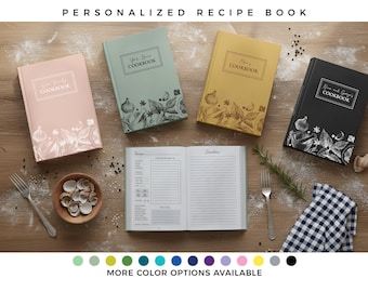 Könnte beinhalten: Eine Sammlung personalisierter Kochbücher in verschiedenen Farben, darunter Rosa, Grün, Gelb und Schwarz. Jedes Buch hat ein einzigartiges Design mit botanischen Illustrationen und dem Text "COOKBOOK". Ein offenes Rezeptbuch ist ebenfalls zu sehen, zusammen mit einer Schale mit Muscheln und einer Gabel.