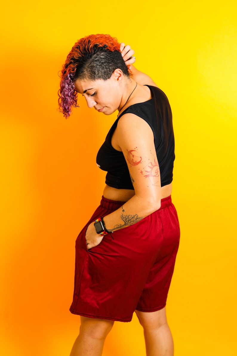 May include: A person wearing a black sleeveless top and burgundy shorts. The person has a tattoo on their arm and is wearing a smartwatch. The background is a gradient of yellow and orange.