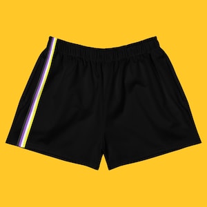 Könnte beinhalten: Schwarze Sporthose mit einem Streifen in den Farben der Non-Binary-Pride-Flagge (weiß, lila, gelb und grau) auf der linken Seite. Die Shorts haben einen elastischen Bund.