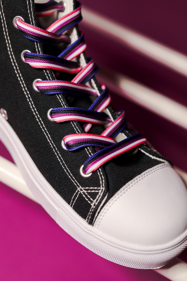 Pode incluir: T&ecirc;nis de lona preto de cano alto com costura branca e biqueira branca. Os cadar&ccedil;os s&atilde;o listrados em vermelho, branco, roxo e azul. O t&ecirc;nis est&aacute; sobre um fundo rosa e branco.