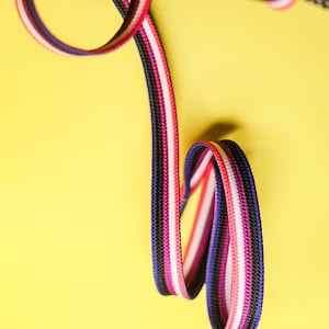 Pode incluir: Close-up de um sapato preto com atacadores coloridos. Os atacadores s&atilde;o uma mistura de preto, branco, rosa, vermelho e azul. O fundo &eacute; amarelo brilhante.
