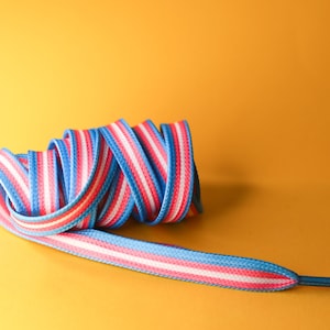 Pode incluir: Um cadar&ccedil;o enrolado com um padr&atilde;o listrado azul, branco e rosa. O cadar&ccedil;o est&aacute; em um fundo amarelo. O cadar&ccedil;o &eacute; um acess&oacute;rio vibrante.