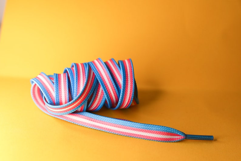 Pode incluir: Um cadar&ccedil;o enrolado com um padr&atilde;o listrado azul, branco e rosa. O cadar&ccedil;o est&aacute; em um fundo amarelo. O cadar&ccedil;o &eacute; um acess&oacute;rio vibrante.
