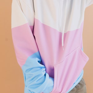 May include: Color block hoodie in white, light blue, and pink. The hoodie features a drawstring hood, a kangaroo pocket, and long sleeves. The sleeves and hood are light blue, the body is white and pink, and the pocket is pink.