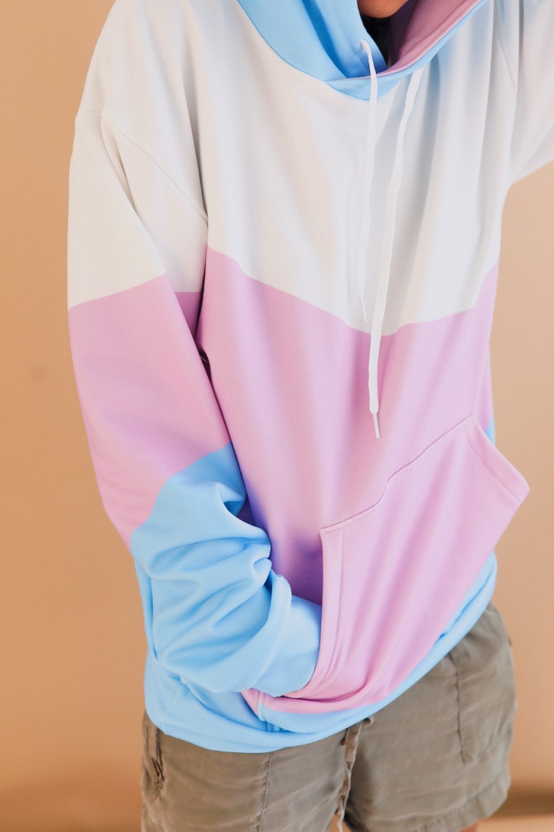 May include: Color block hoodie in white, light blue, and pink. The hoodie features a drawstring hood, a kangaroo pocket, and long sleeves. The sleeves and hood are light blue, the body is white and pink, and the pocket is pink.