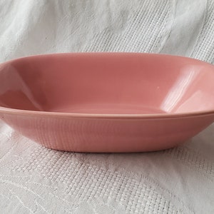 Puede incluir: Un plato para hornear ovalado de cerámica rosa con una textura ligeramente ondulada. El plato tiene un acabado liso y brillante y es perfecto para servir o hornear.